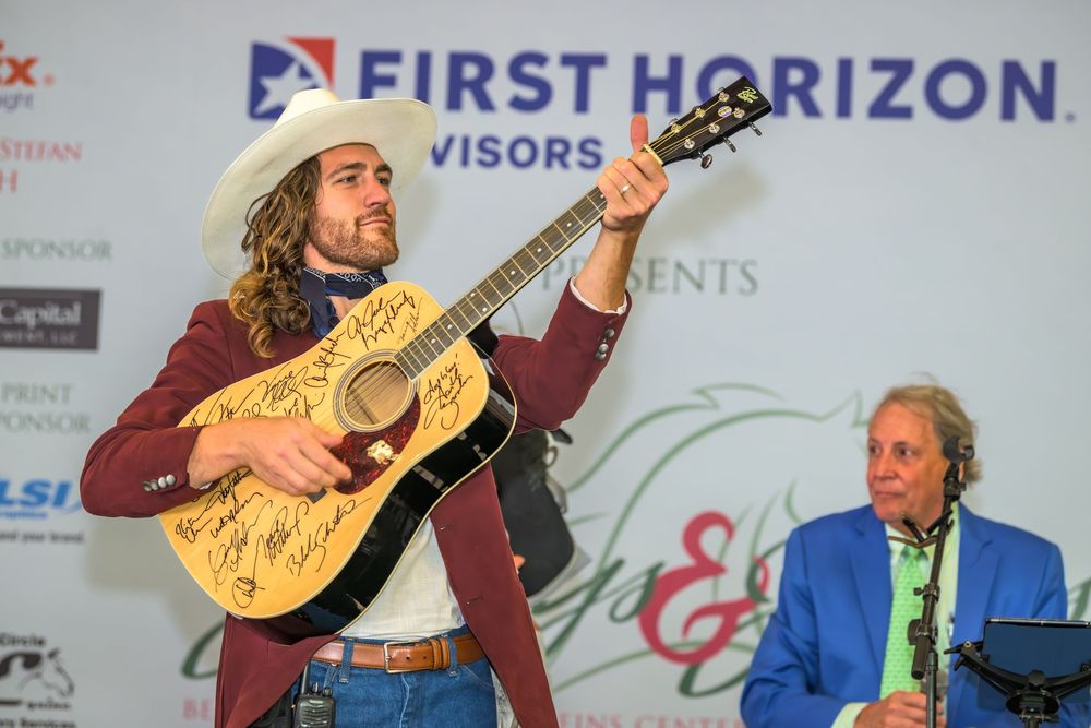 A musician performs on stage with a decorated acoustic guitar at a First Horizon sponsored event.