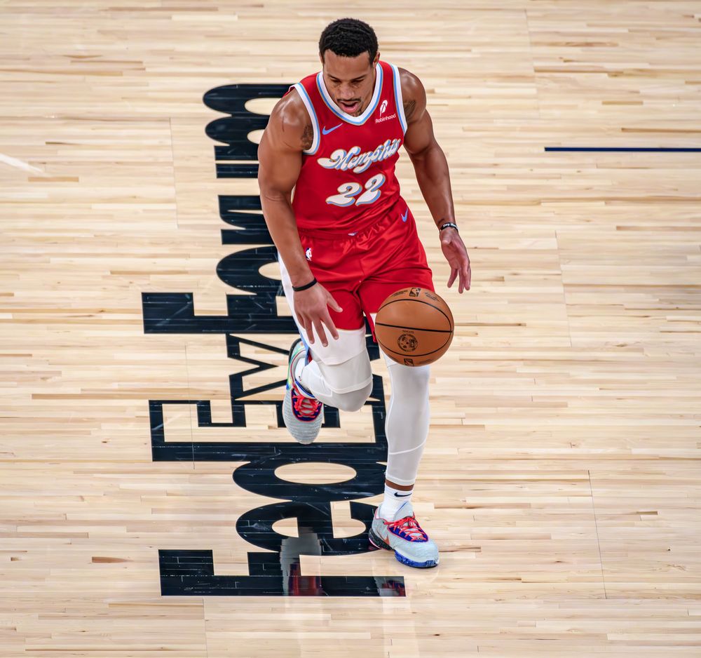 Basketball player dribbles on hardwood court during game while wearing red and white uniform.