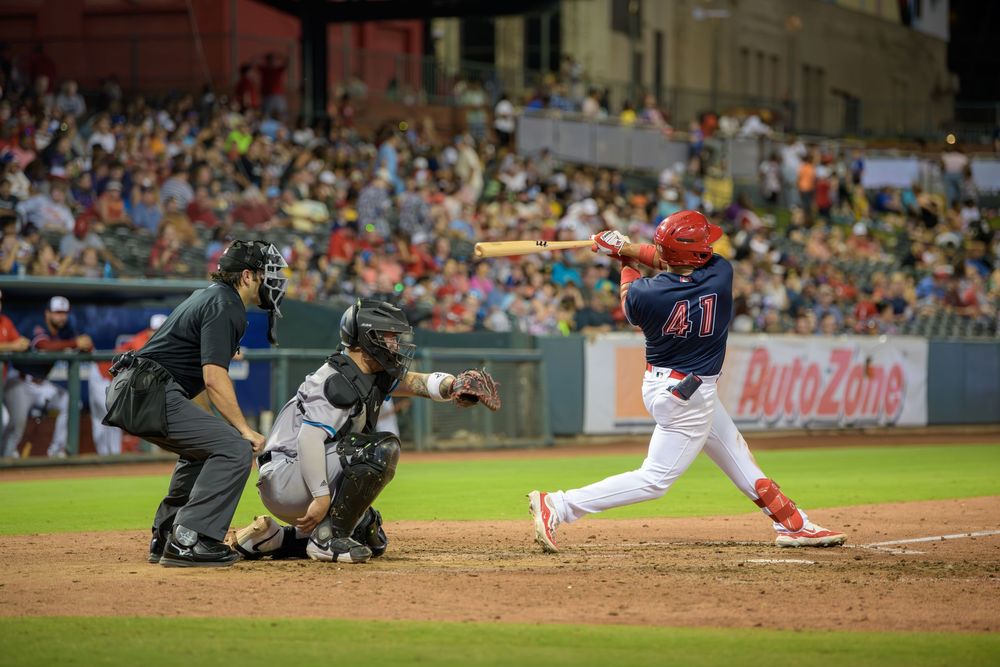 Baseball player slides into base during intense game action while fielder attempts to make the tag.