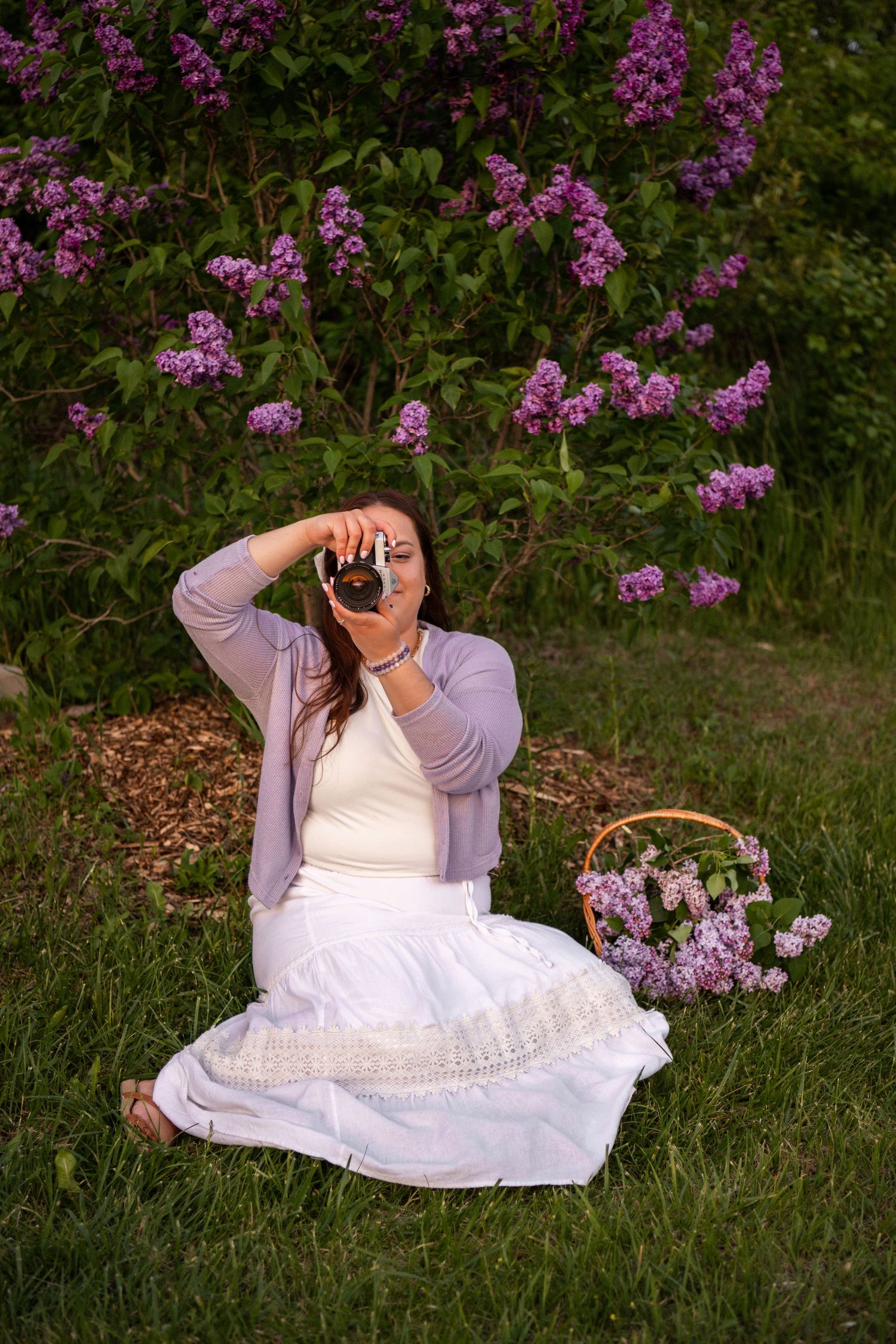 Photographer in white dress capturing photos among purple wildflowers.