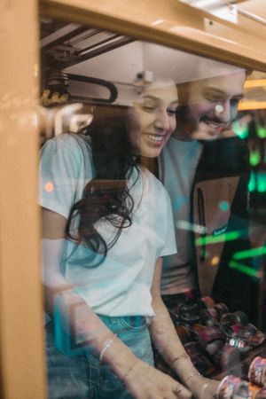 Two young people smiling and laughing together while looking at an arcade game machine.