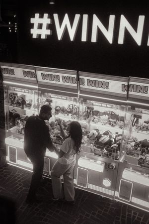 Black and white photo of a couple playing a claw machine arcade game at night under a WIN sign.