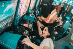 Woman smiling while playing a racing arcade game with a man in a vibrant arcade.