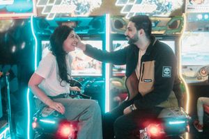 Couple laughing and bonding while sitting on motorcycle arcade games in a colorful arcade.