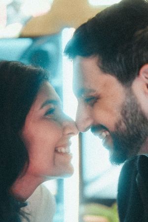 A smiling couple faces each other closely, sharing an intimate moment with warm lighting in the background.