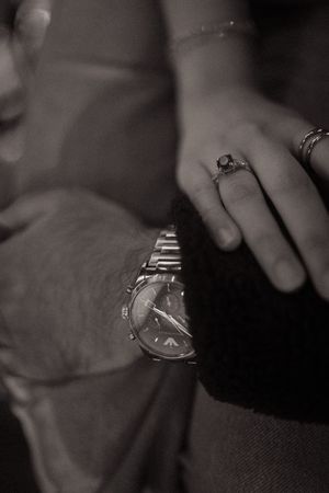 Black and white close-up of a couple's hands, woman wearing rings, man wearing a classic silver wristwatch.