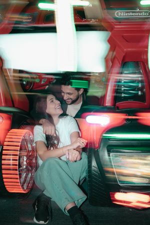 Couple smiling and holding hands beside colorful bumper cars at a Nintendo-themed amusement arcade.