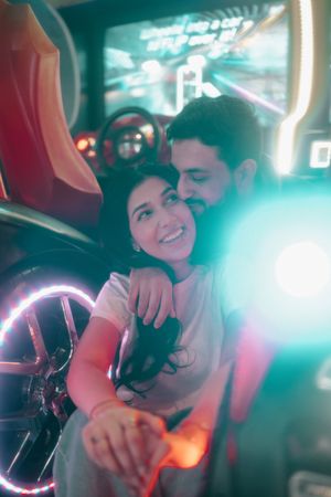 A couple shares a romantic moment at an arcade game, smiling together under colorful neon lights.
