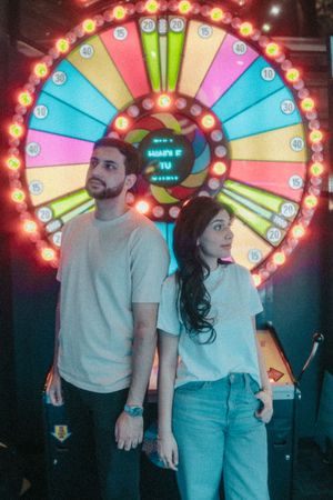 Couple standing back-to-back in front of a colorful illuminated prize wheel at an arcade.