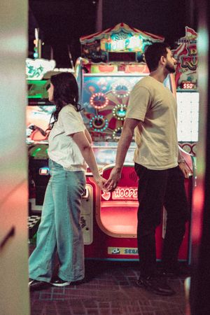 Couple holding hands in an arcade, standing in front of colorful SEGA gaming machines in a dimly lit venue.