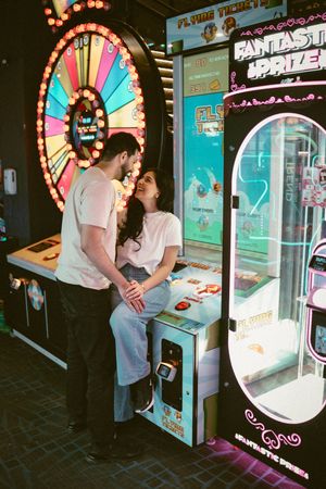 Romantic couple sharing a tender moment beside arcade games with a prize wheel backdrop.