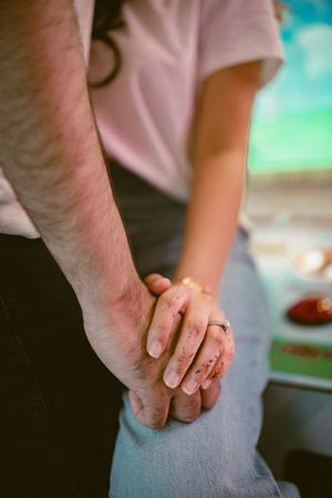 Close-up of a couple holding hands, woman wearing a ring, sitting together in a warm, intimate moment.