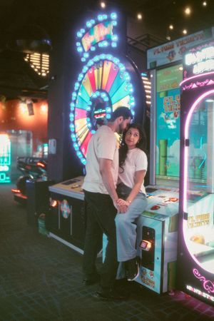 Couple sharing a romantic moment at a colorful arcade, surrounded by neon lights and classic gaming machines.