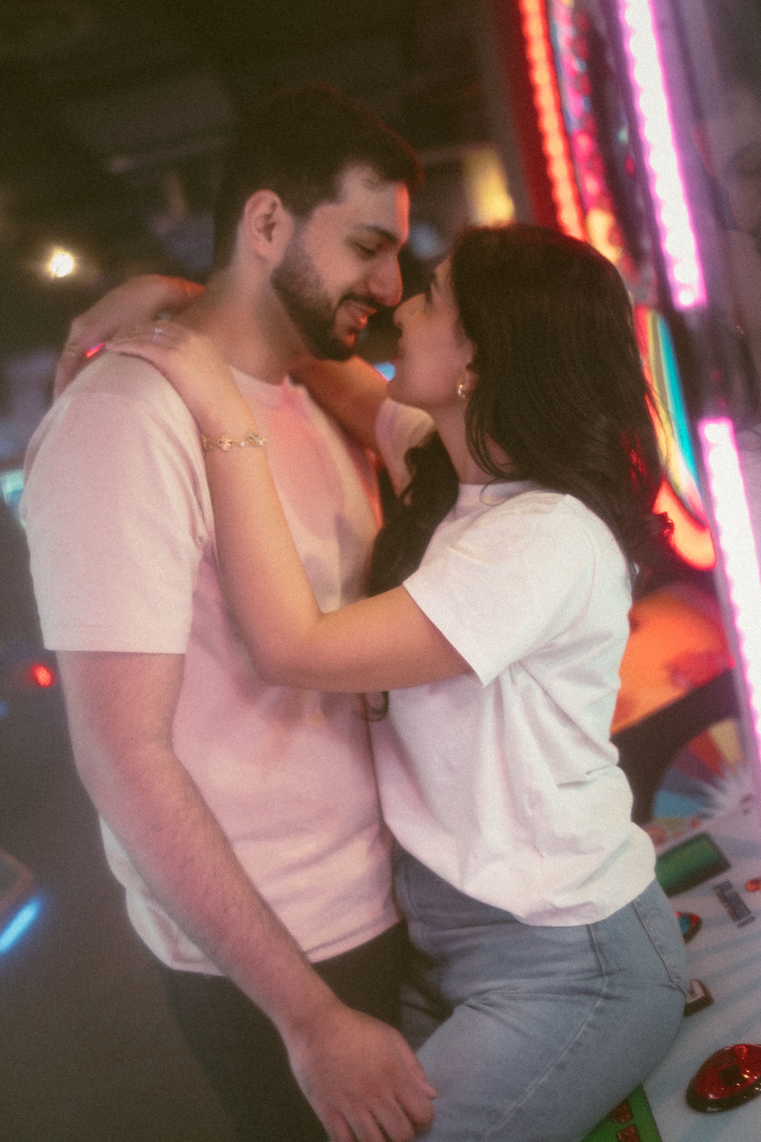 Romantic couple embracing and smiling at each other under colorful neon lights in a vibrant venue.