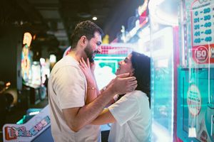 Romantic couple sharing a tender moment in a colorful arcade, surrounded by glowing neon game machines.