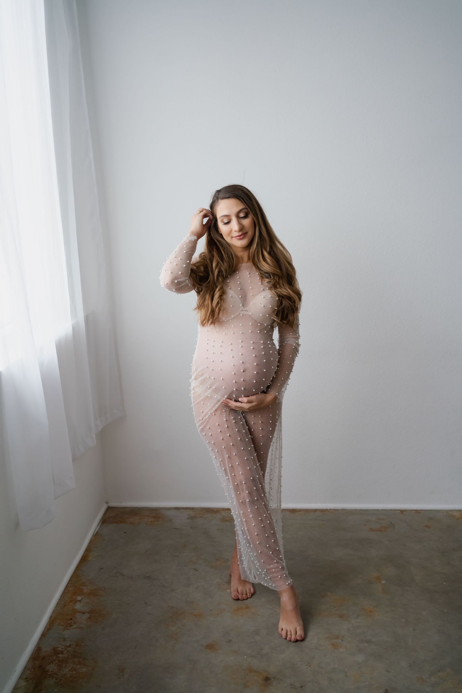 Maternity photo shoot in cozy pink knit dress against minimalist grey backdrop.