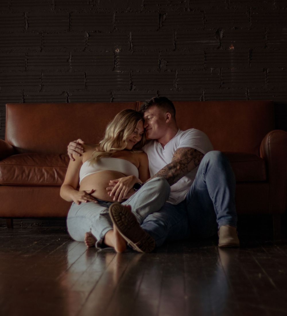 A romantic low-light portrait on a leather couch against dark brick walls.