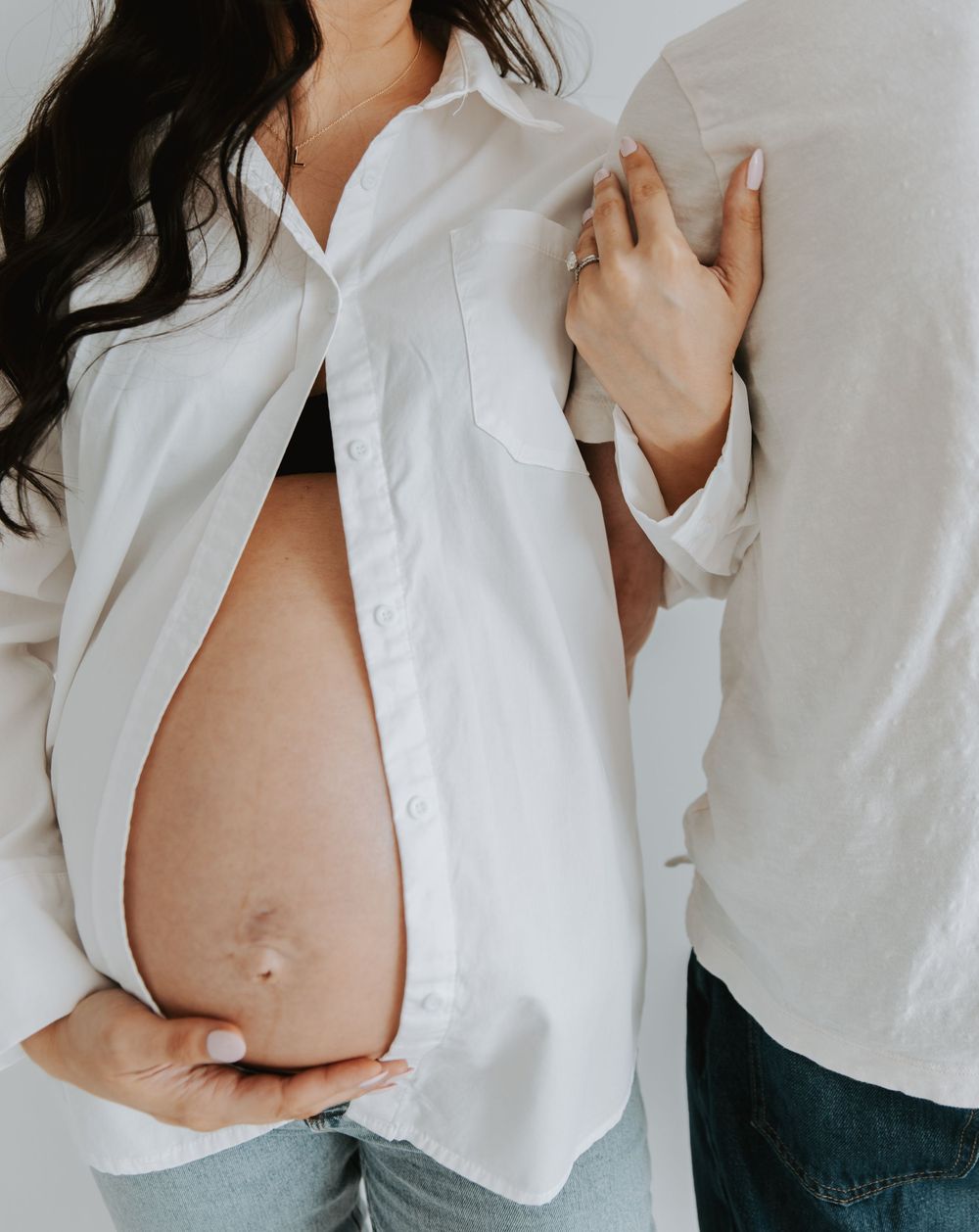 A maternity photo featuring an open white button-down shirt revealing a pregnant belly.