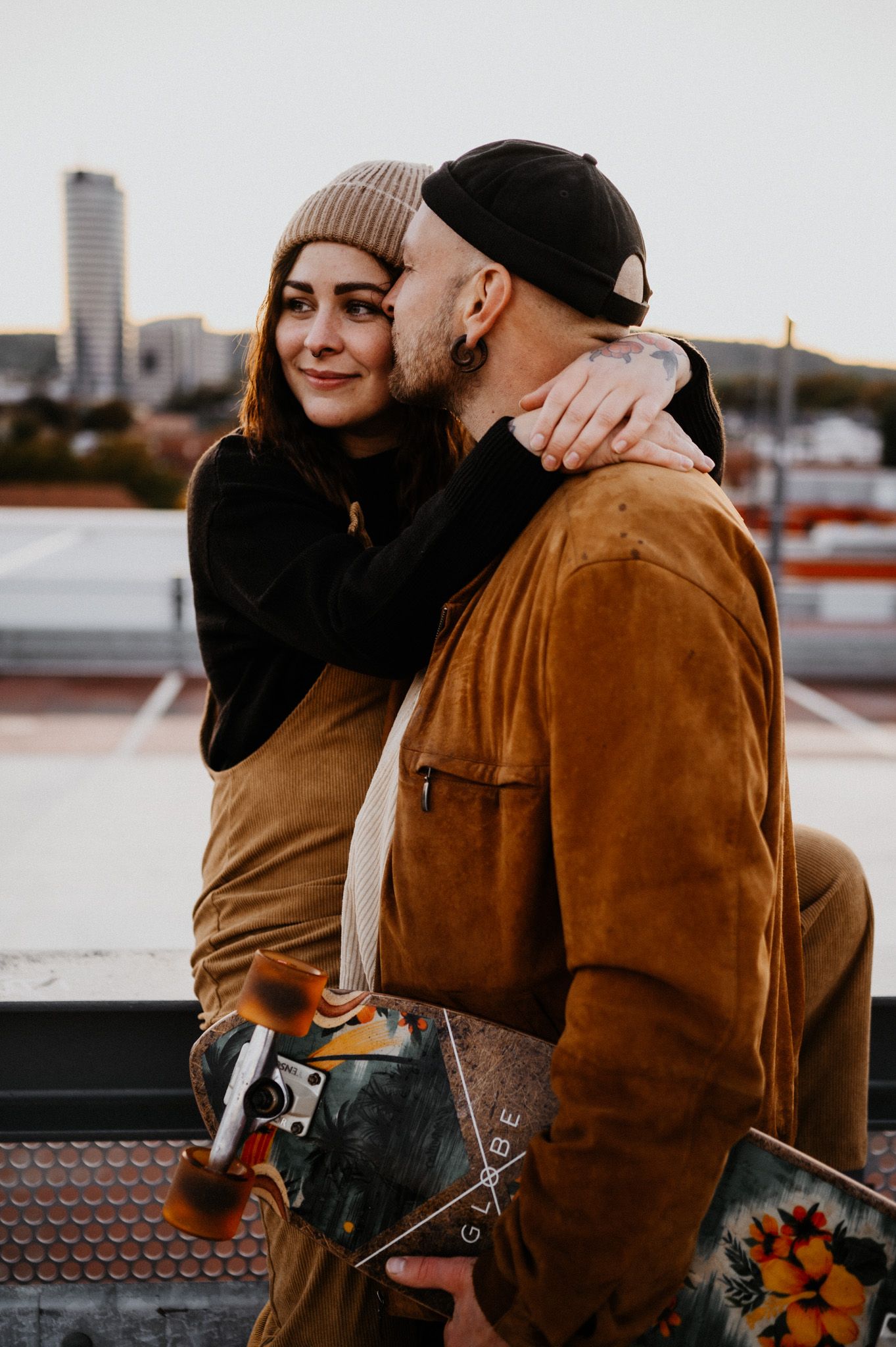 Urban rooftop scene with couple in casual wear against city backdrop at sunset.