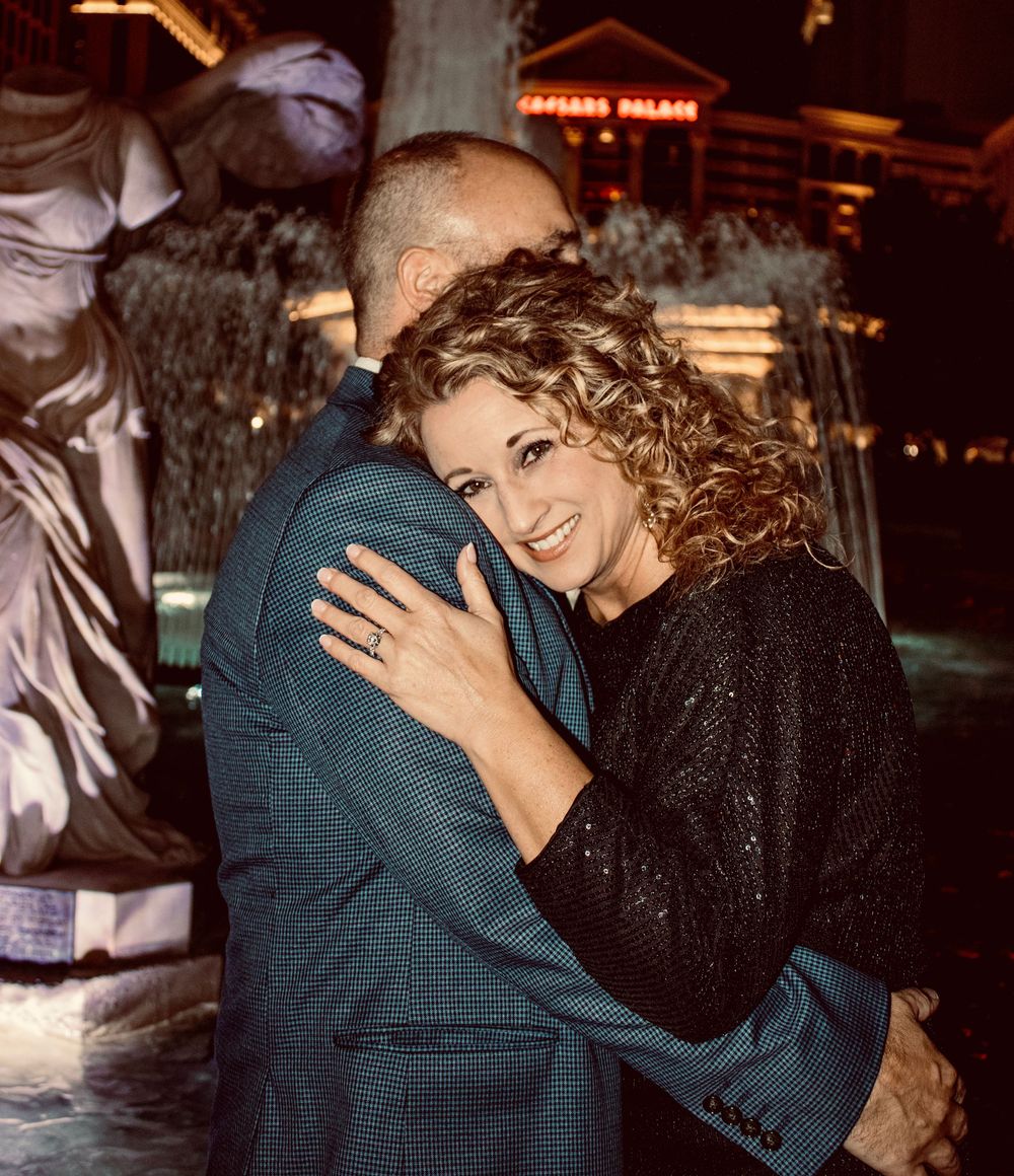 Woman smiling joyfully while embracing a man outside Caesars Palace in Las Vegas at night.
