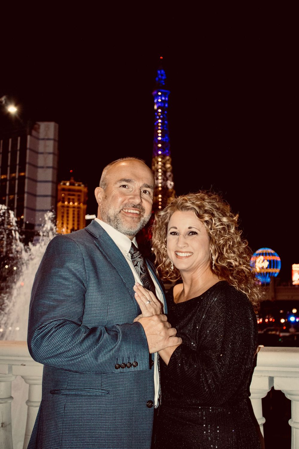 Happy couple embracing on the Las Vegas Strip at night with the Paris Hotel tower glowing behind them.