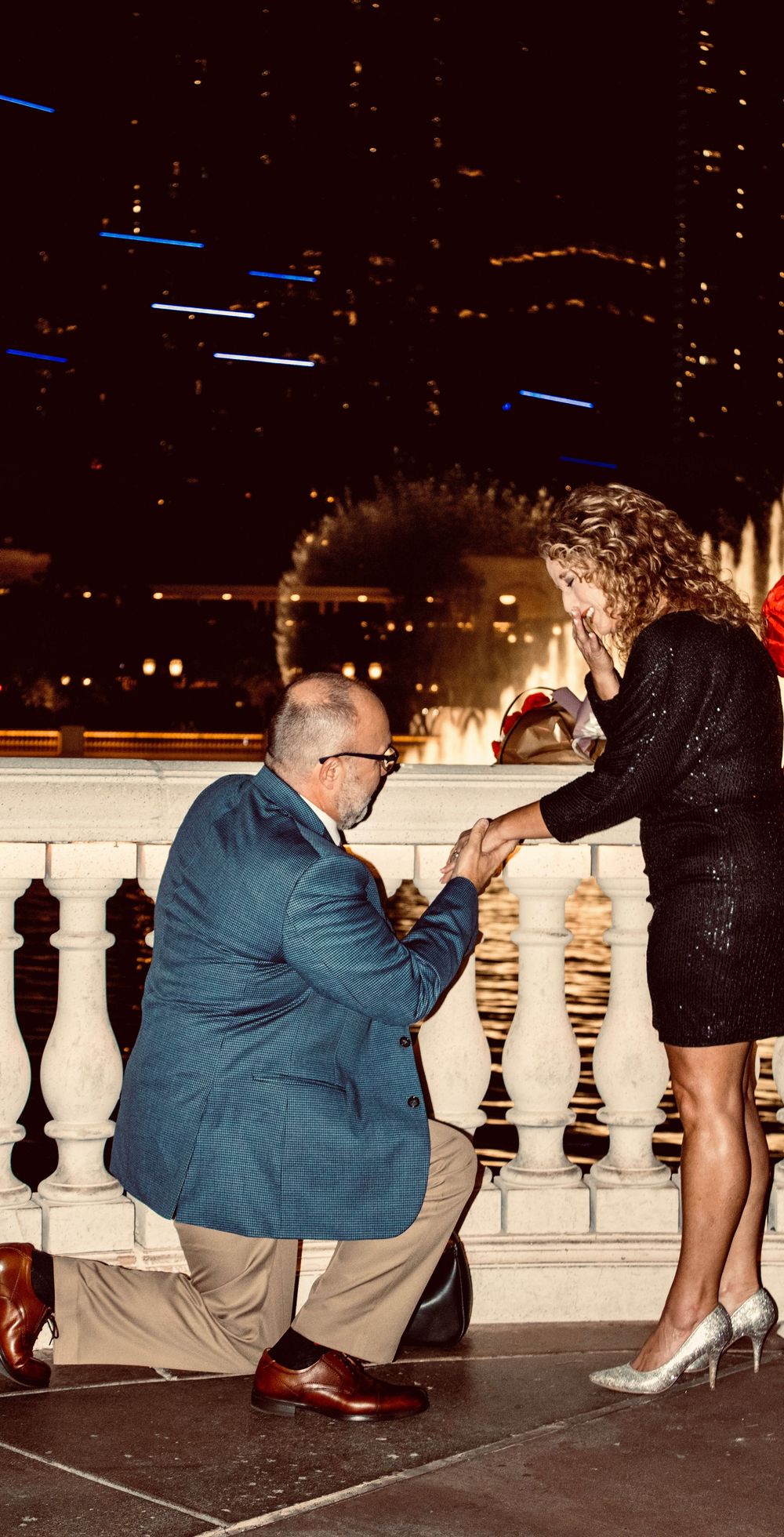 Man proposing on one knee to a woman at the Bellagio fountains in Las Vegas at night.