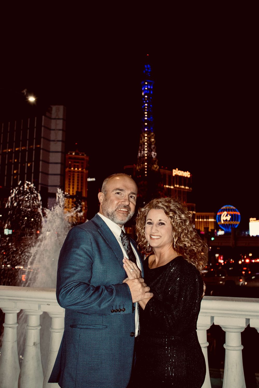 Couple posing at night on the Las Vegas Strip with the Eiffel Tower replica illuminated behind them.