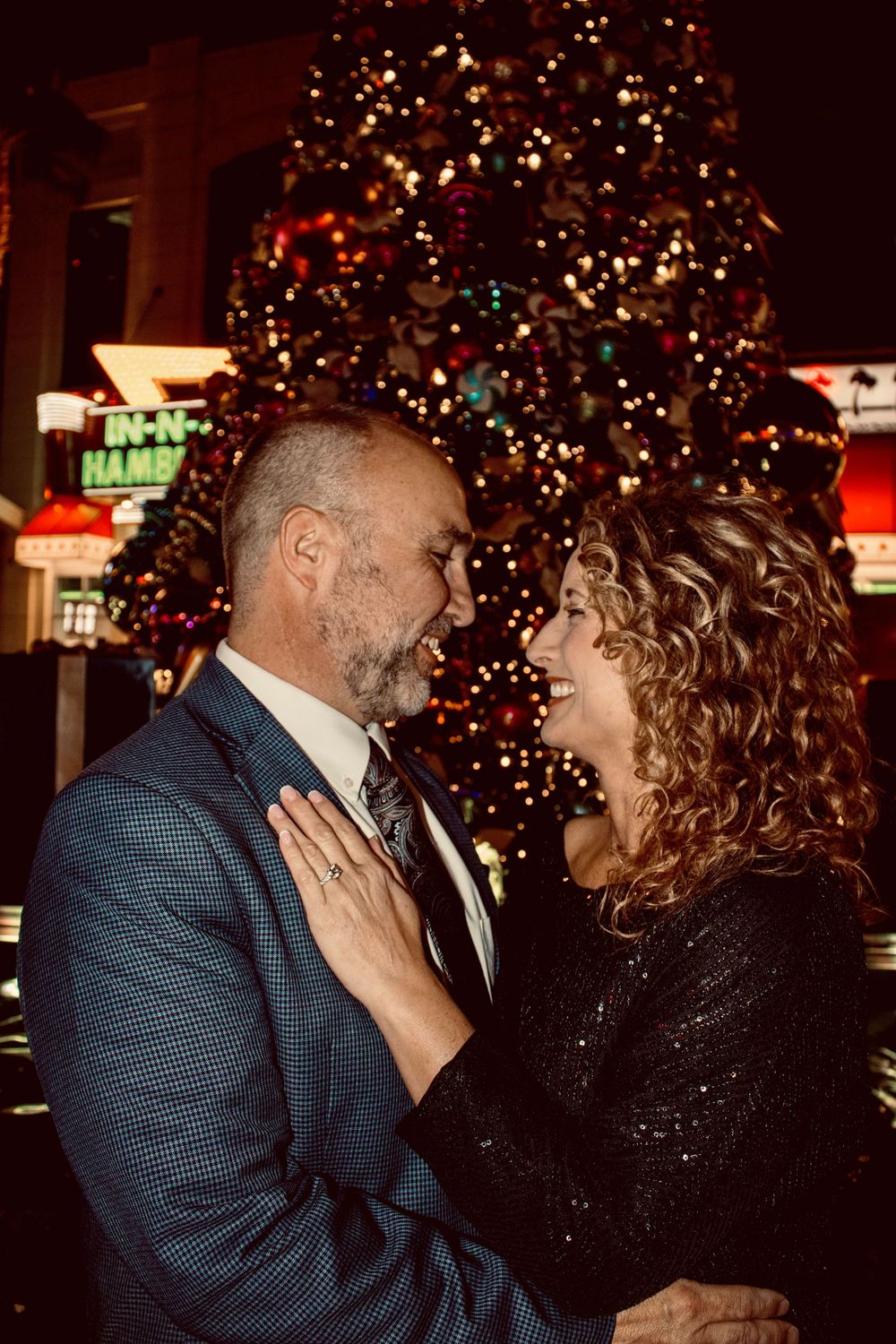 Couple sharing a romantic moment in front of a lit Christmas tree on the Las Vegas Strip at night.