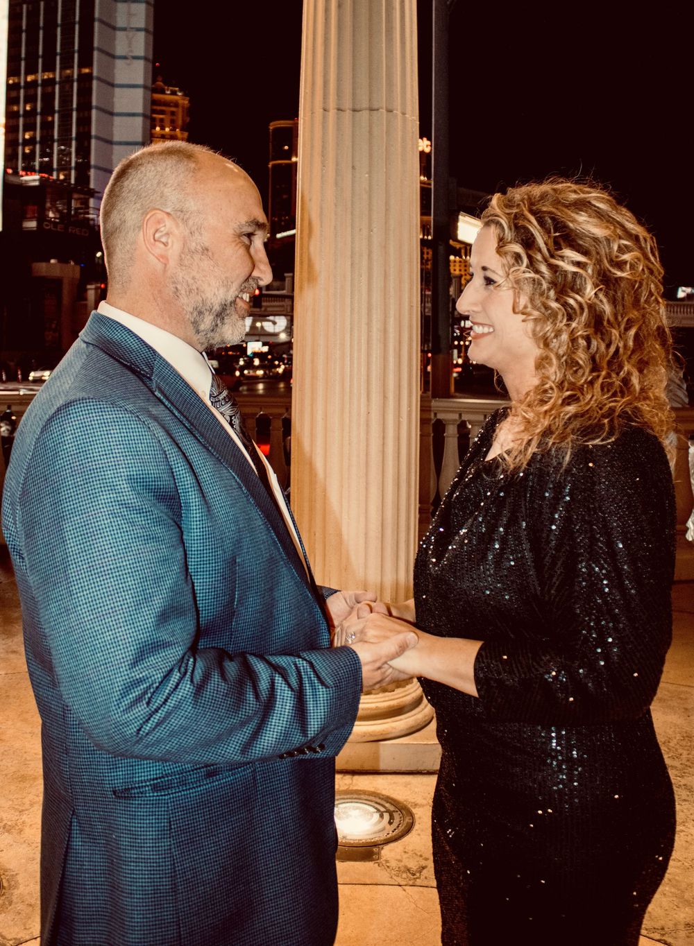 Newly engaged couple holding hands and gazing at each other on the Las Vegas Strip at night.