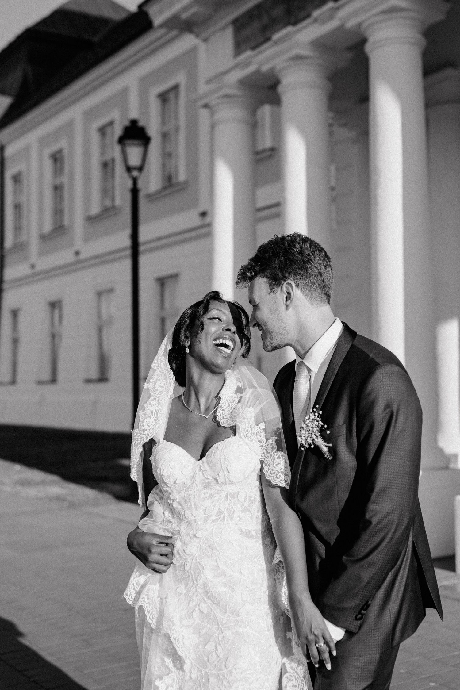 A black and white portrait of newlyweds sharing a loving moment against a classical columned building.