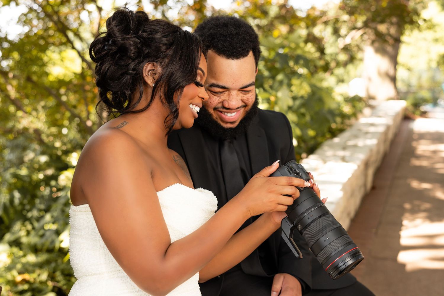 A happy couple laughs together during a romantic outdoor photo session in a sunlit park setting.