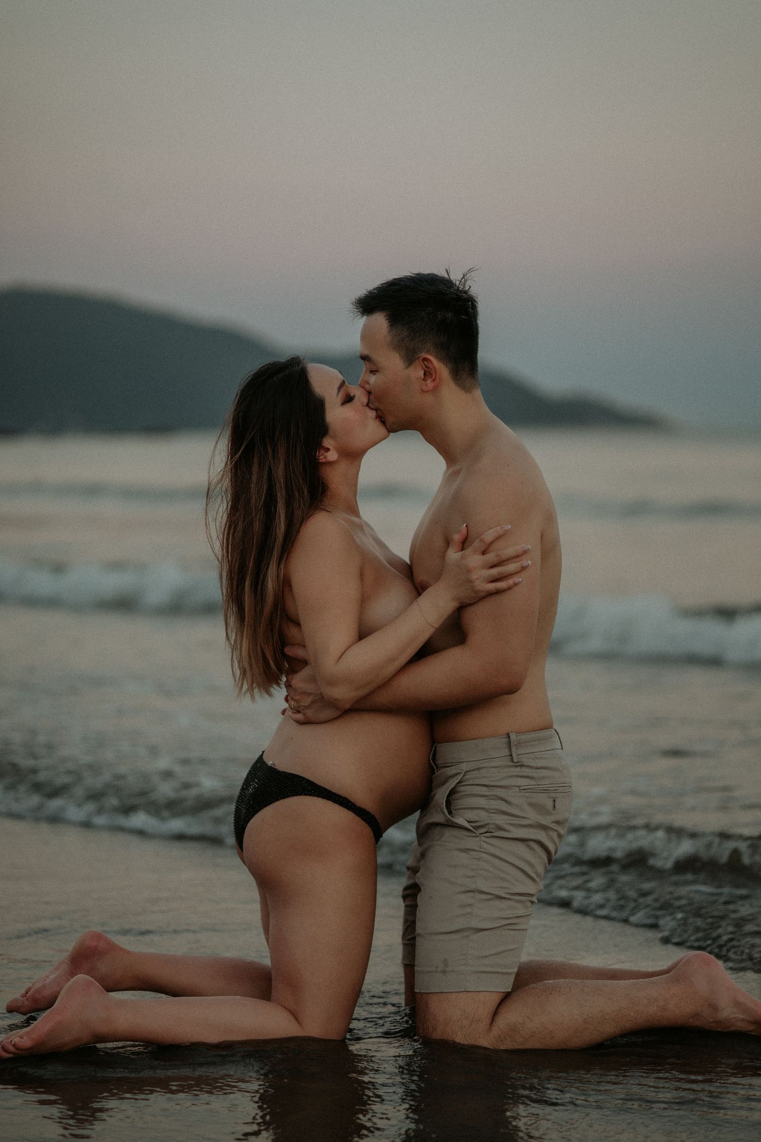 Romantic couple sharing intimate moment on sandy beach at dusk.