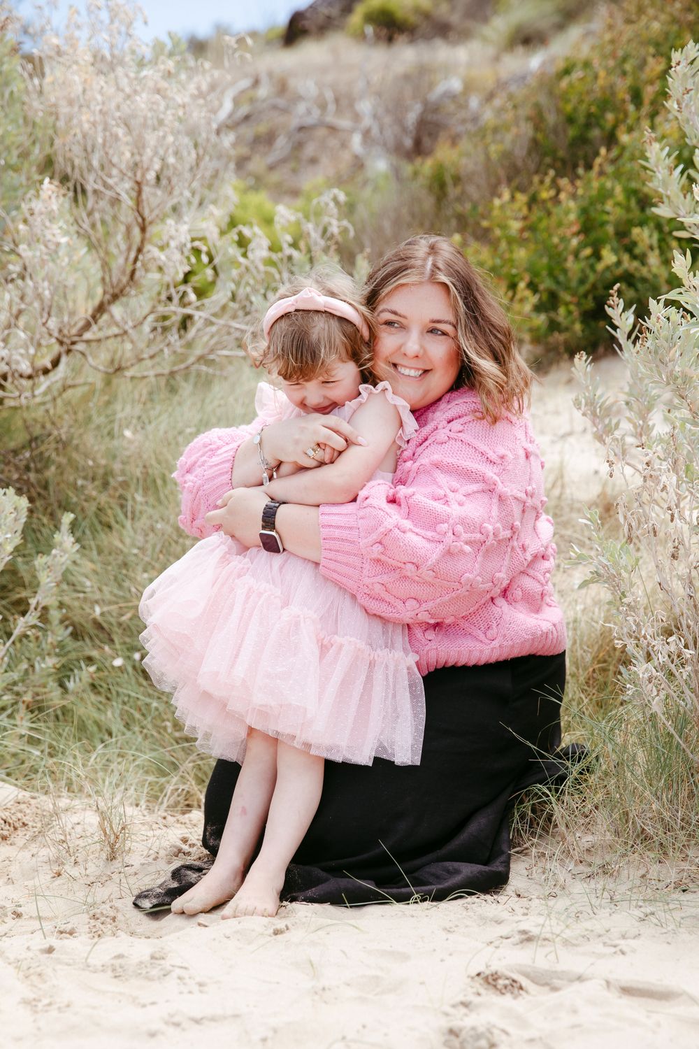 Tender moment captured in nature with pink outfits against green foliage.