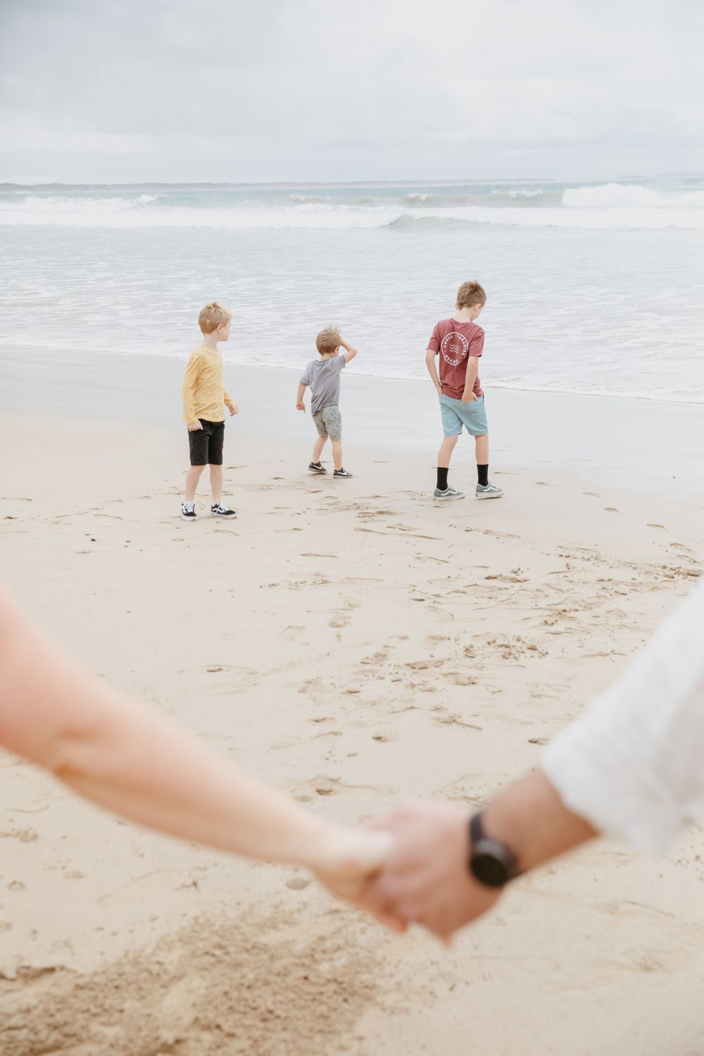 Three people walking on beach with waves while parents hold hands in foreground.