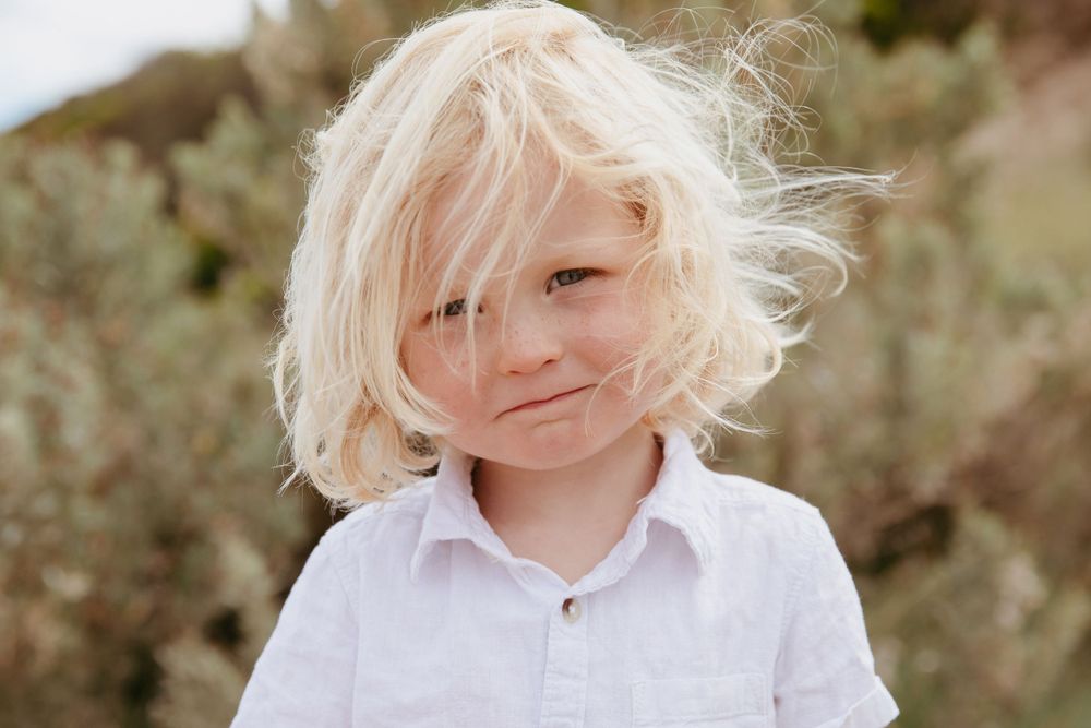 Portrait of young person with windswept blonde hair wearing white shirt outdoors.