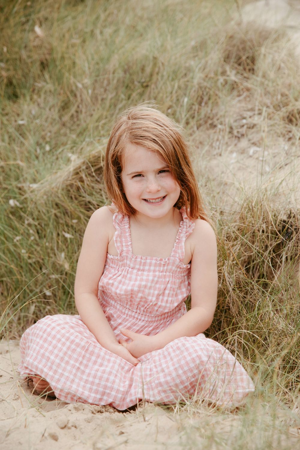 Young person in pink gingham dress sitting in tall grass with natural lighting.