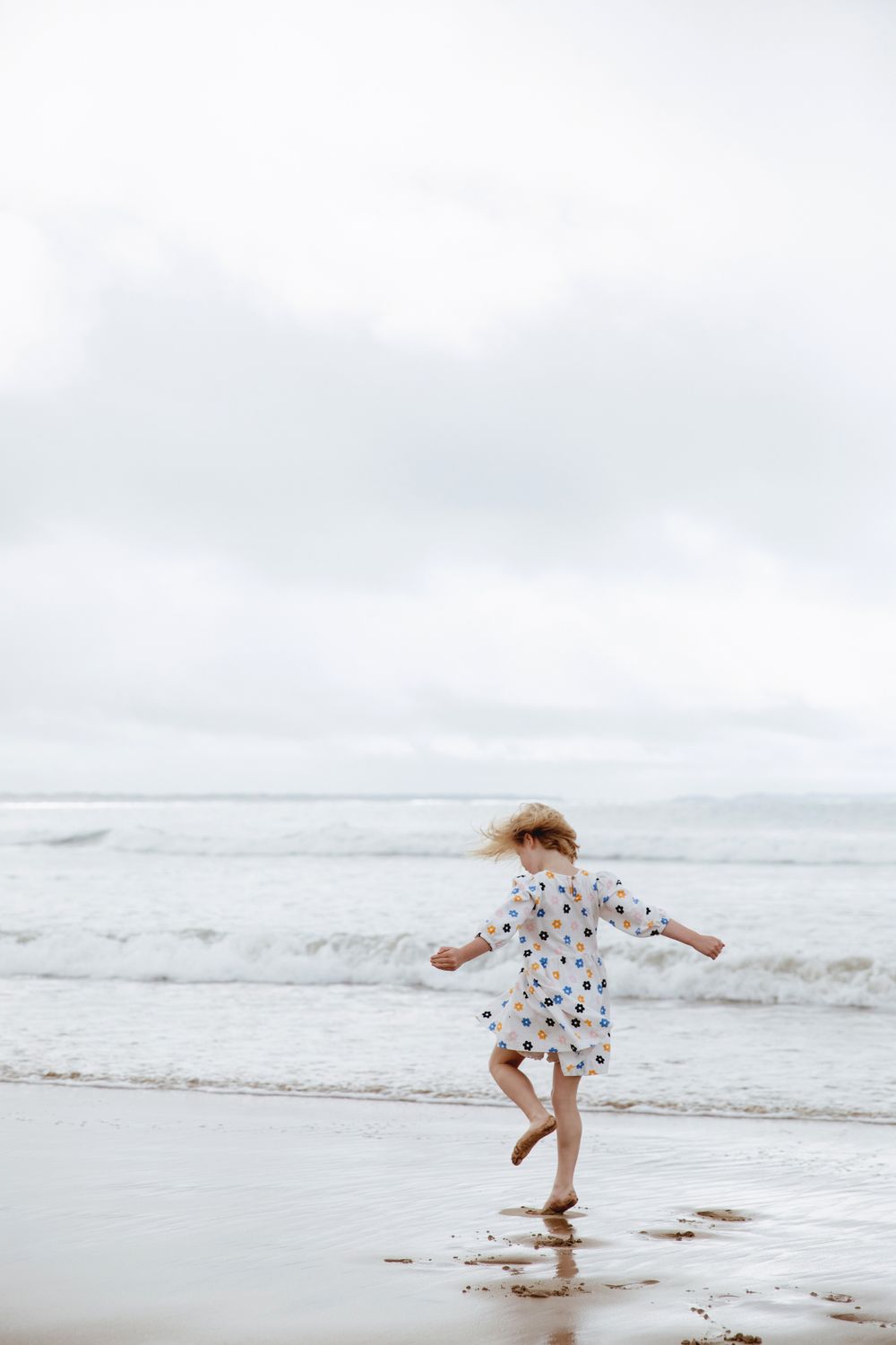 Child in polka dot dress dancing on beach with waves in background.