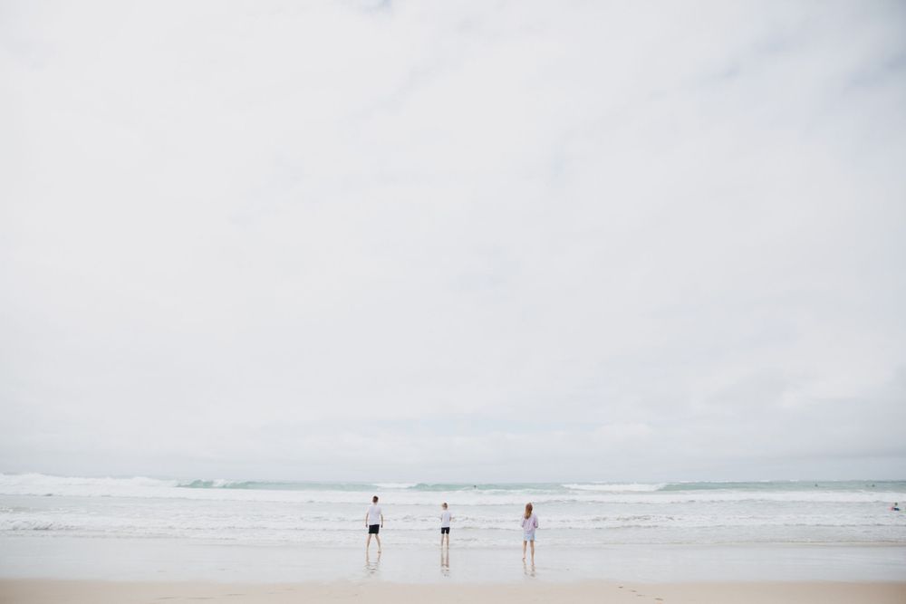 Three distant figures walking along a misty beach with overcast sky.