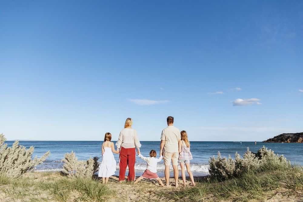 Family enjoying a sunny day at the beach with clear blue skies and sand dunes in the background.