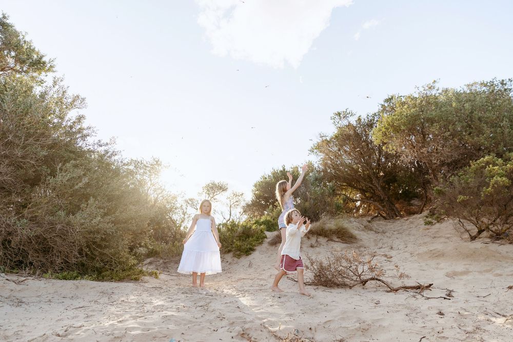 Two people in white dresses dance joyfully on a sandy beach path during golden hour.