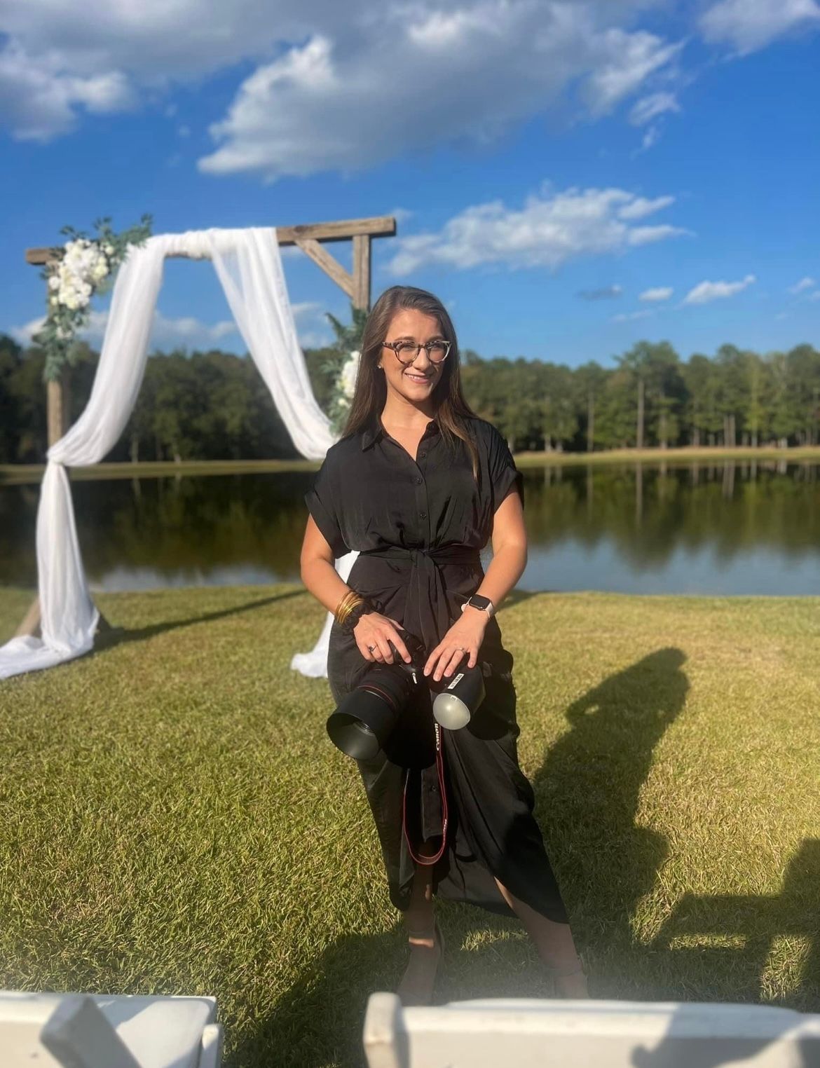 Outdoor photoshoot setup by a lake with white drapes and props on green grass.