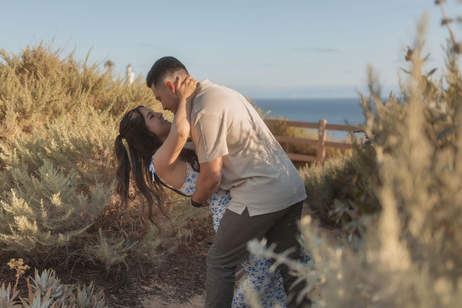 Couple embracing among greenery with the ocean in the background.