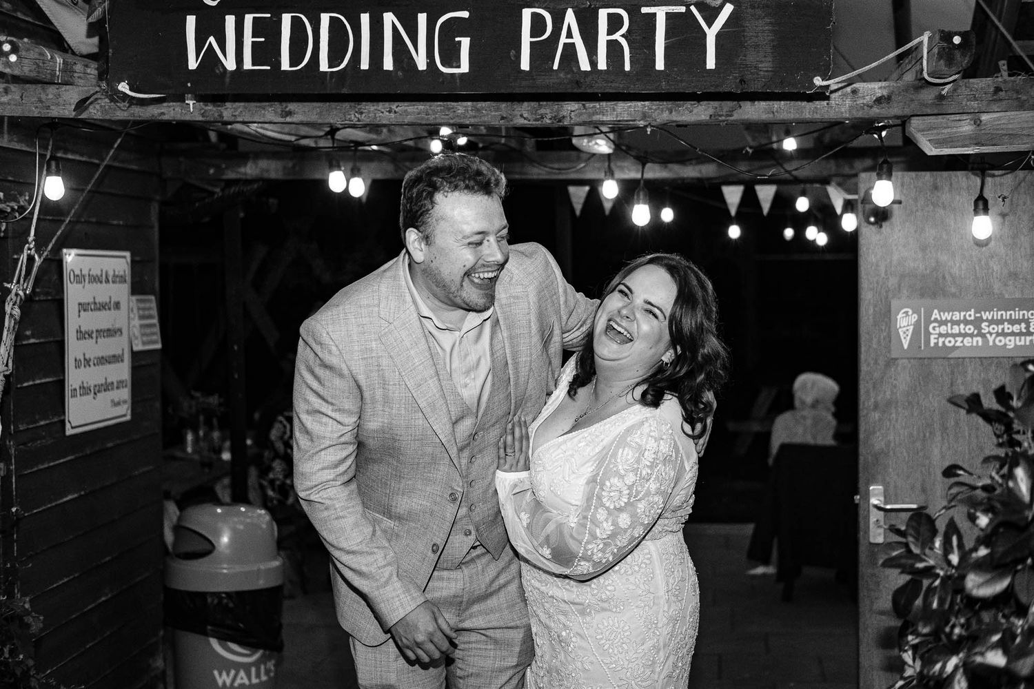 Rustic wedding party sign hangs above celebration with string lights creating warm ambiance.