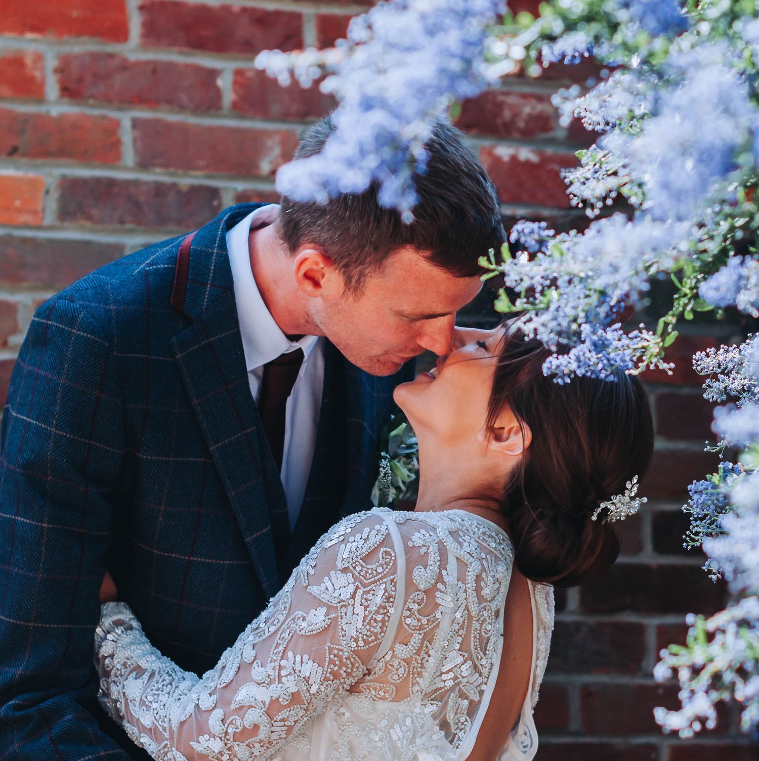 Romantic moment against a brick wall with blooming lilac flowers in the background.