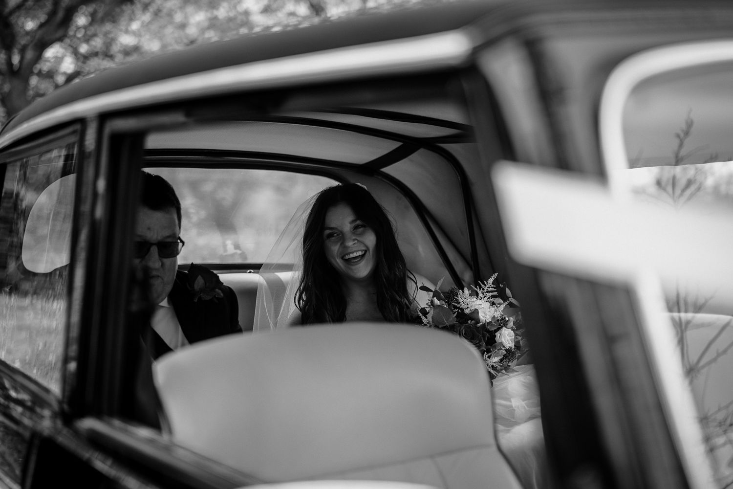 Wedding day moment captured through a car window creating a cinematic effect.