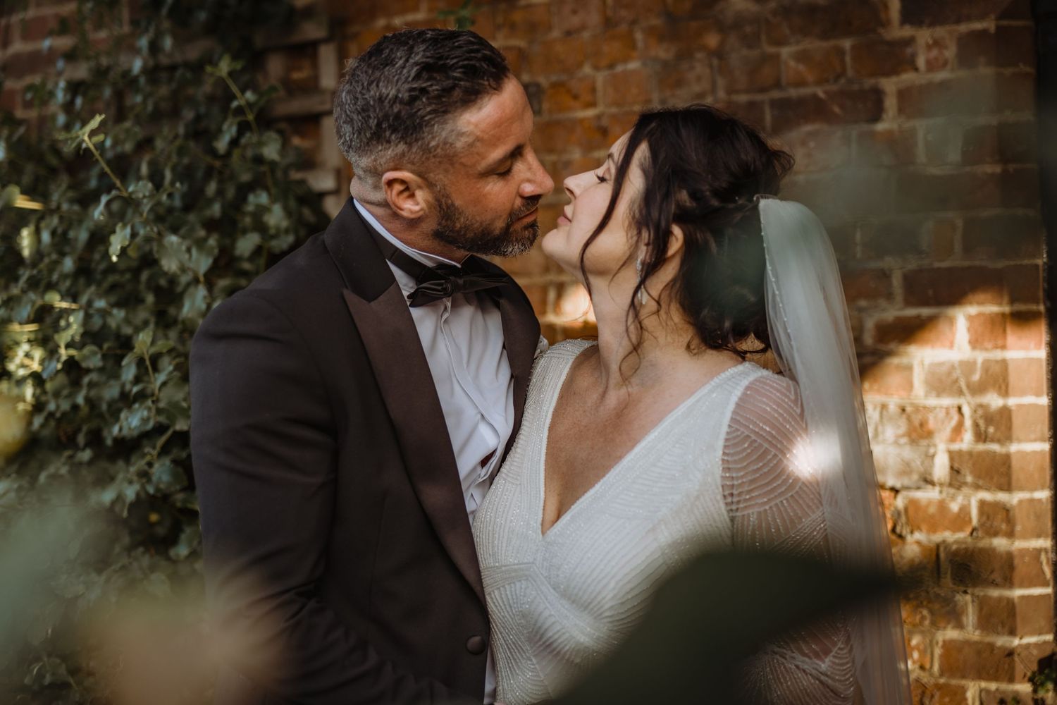 A romantic moment between newlyweds against a rustic brick wall backdrop.
