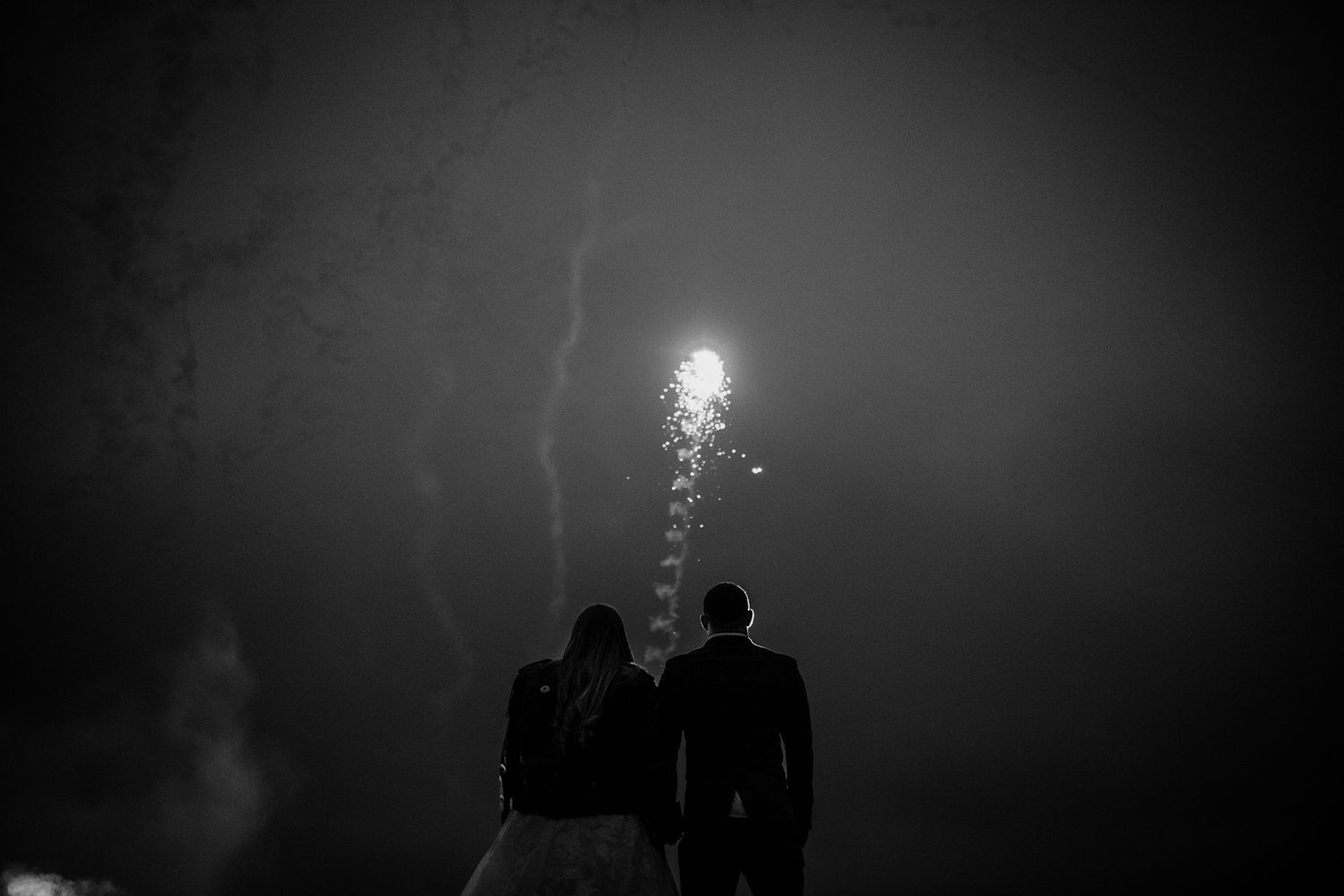 Dramatic nighttime silhouettes against dark sky at outdoor wedding celebration.