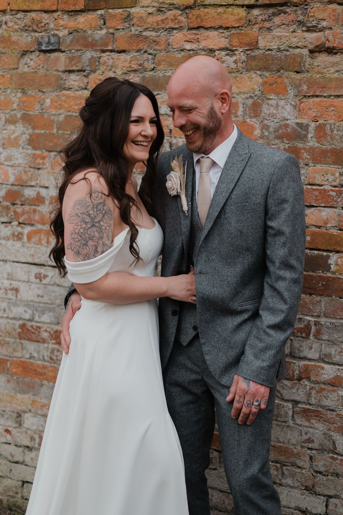 Couple sharing intimate moment against rustic brick wall at wedding venue.