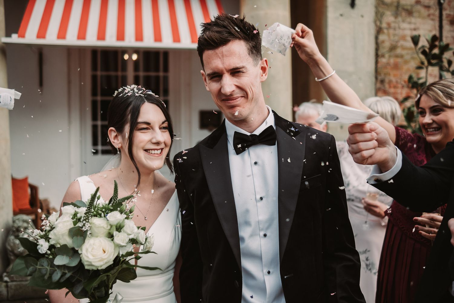 Wedding party celebrating with confetti and laughter outside venue.