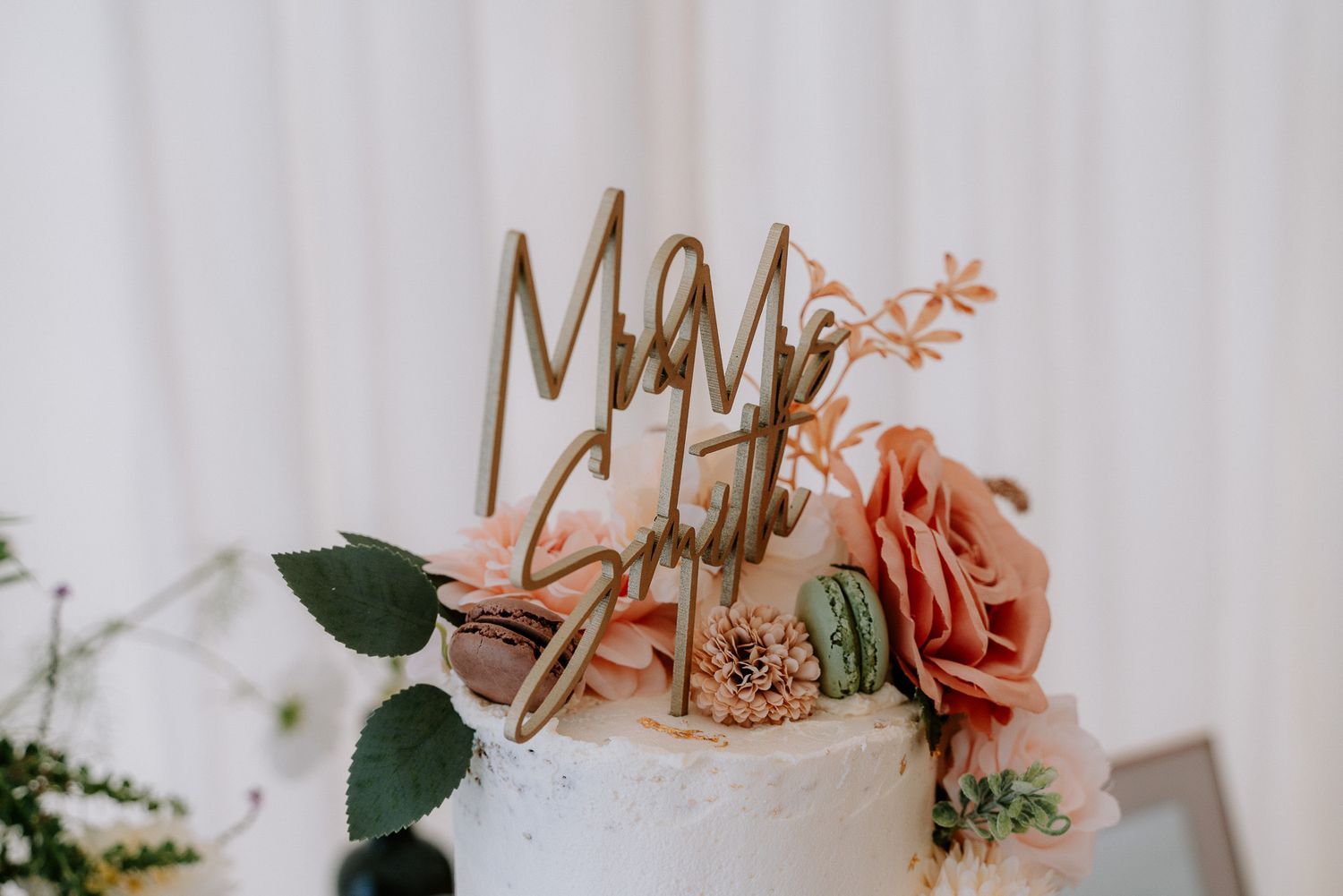 Elegant wedding cake decorated with pink roses and floral accents on white backdrop.